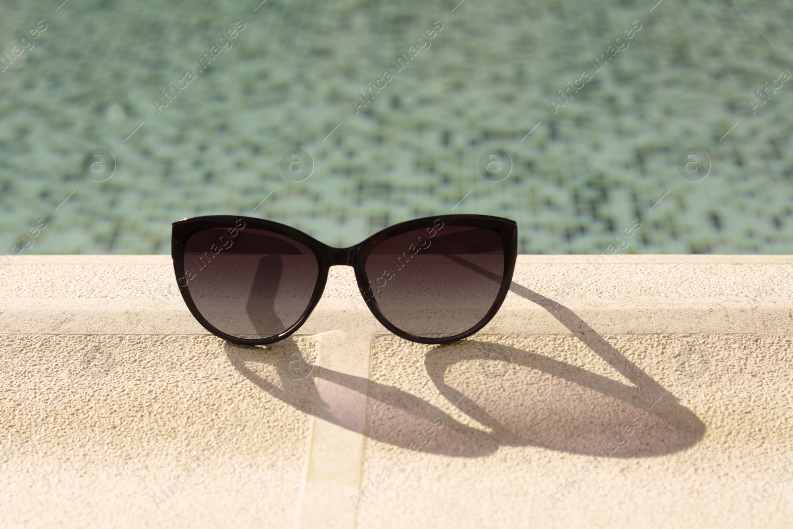 Photo of Stylish sunglasses near outdoor swimming pool on sunny day, space for text