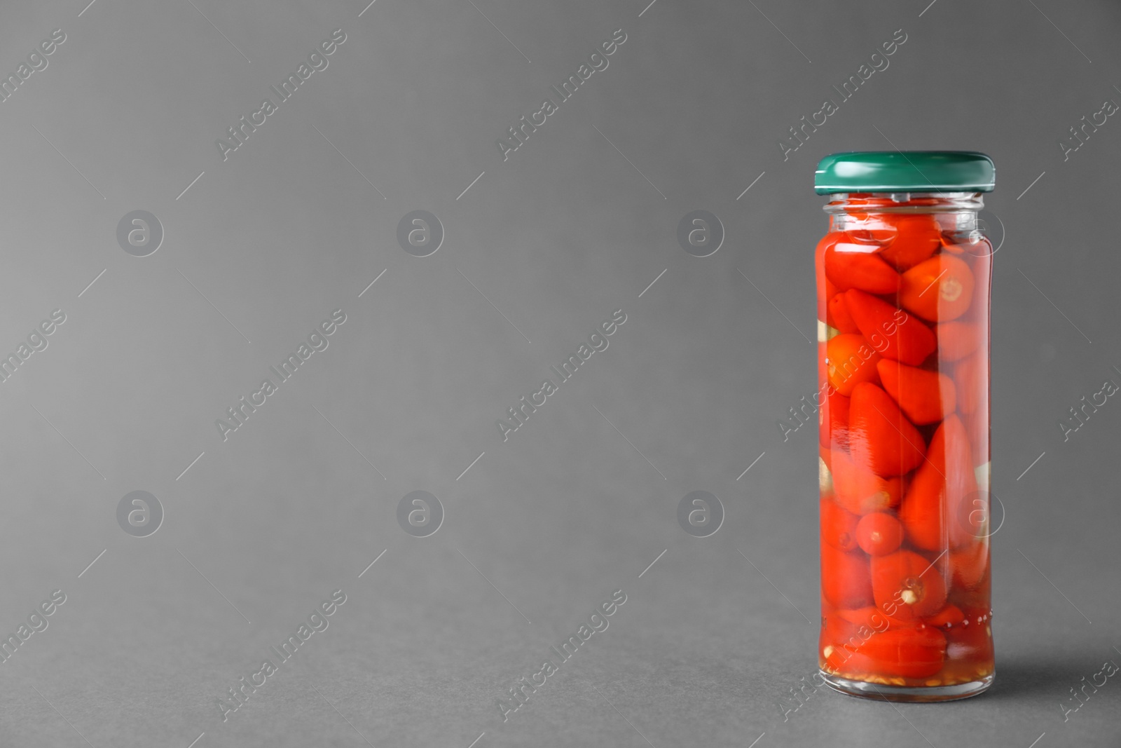 Photo of Jar of pickled red hot piri-piri peppers on grey background. Space for text