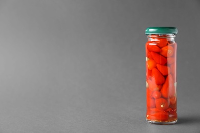 Photo of Jar of pickled red hot piri-piri peppers on grey background. Space for text