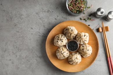 Wooden plate with tasty baozi dumplings and sesame seeds served on grey table, top view. Space for text