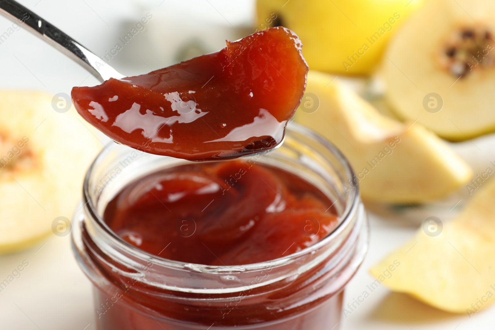 Photo of Taking tasty homemade quince jam from jar at table, closeup