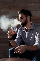 Photo of Man with glass of whiskey and cigar sitting at table indoors