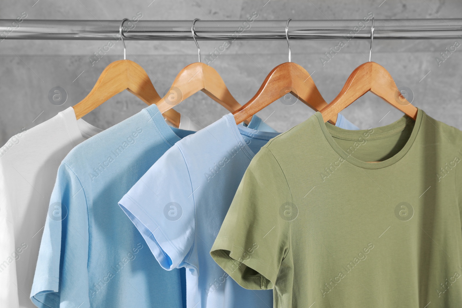 Photo of Different clean T-shirts hanging on rack near grey wall