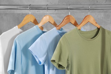 Photo of Different clean T-shirts hanging on rack near grey wall