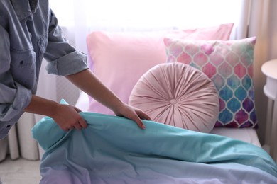 Photo of Woman making bed with new linens in children's room, closeup. Modern interior design