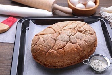 Photo of Baking pan with parchment paper and tasty homemade bread on wooden table