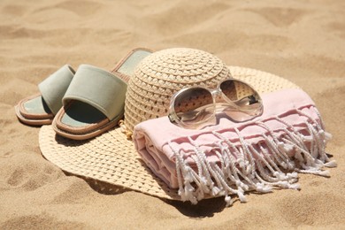 Photo of Straw hat, sunglasses, towel and slippers on sand, closeup. Beach accessories