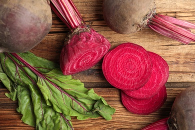 Photo of Cut and whole raw beets on wooden table, flat lay