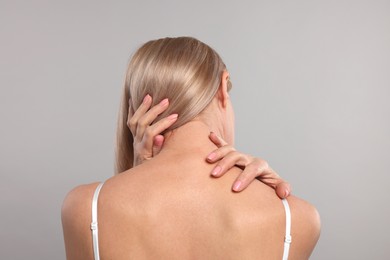 Woman suffering from pain in her neck on grey background, back view