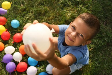 Little boy with water bombs on green grass, top view