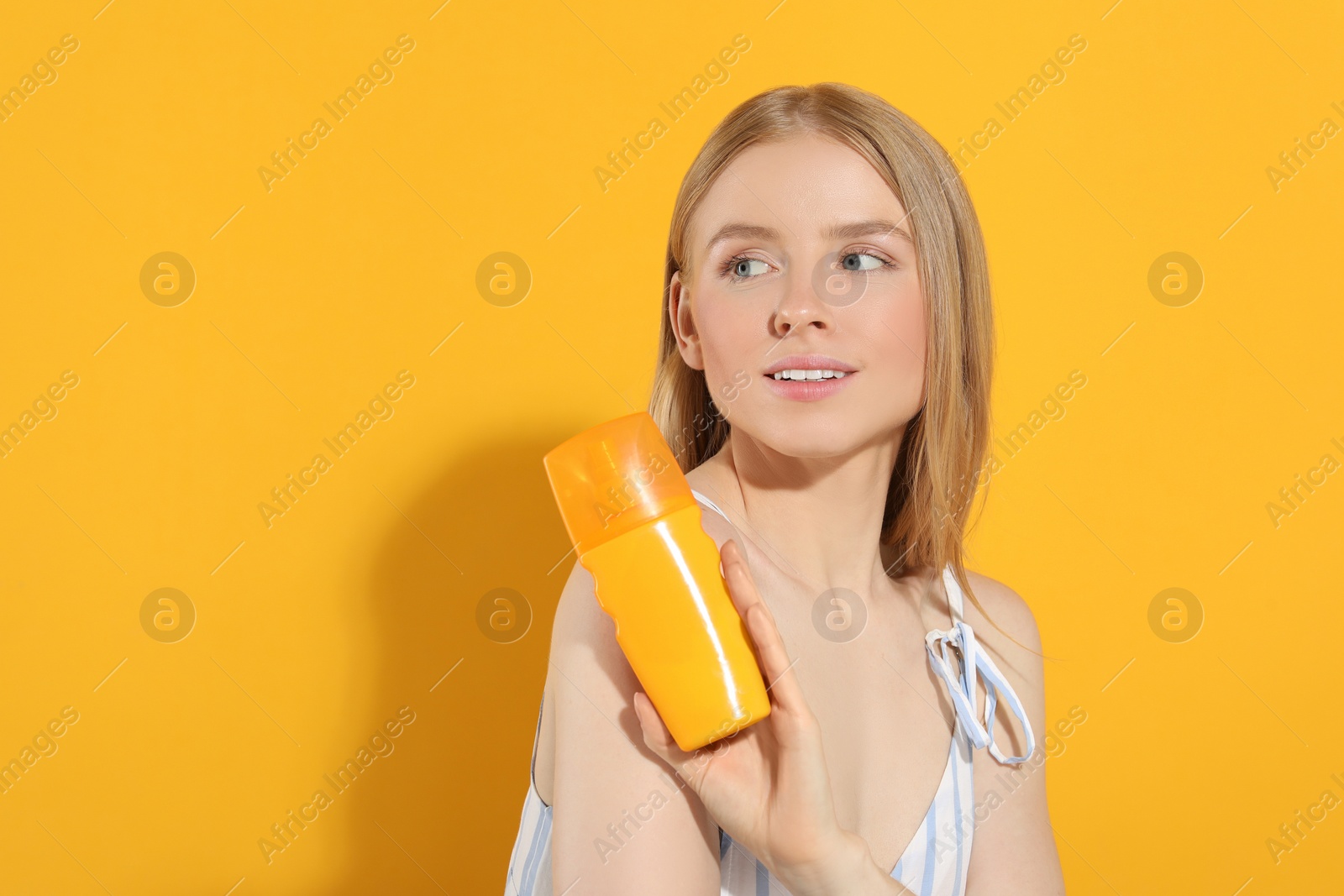 Photo of Beautiful young woman holding sun protection cream on orange background, space for text