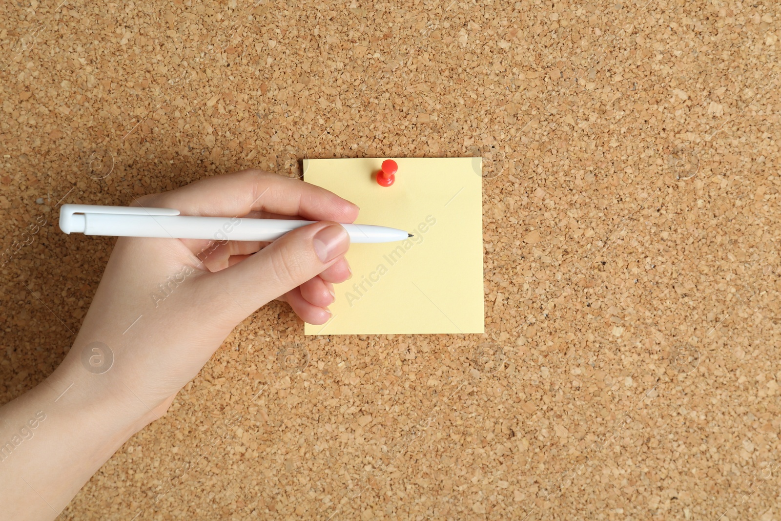 Photo of Woman writing on sticky note pinned to corkboard, closeup