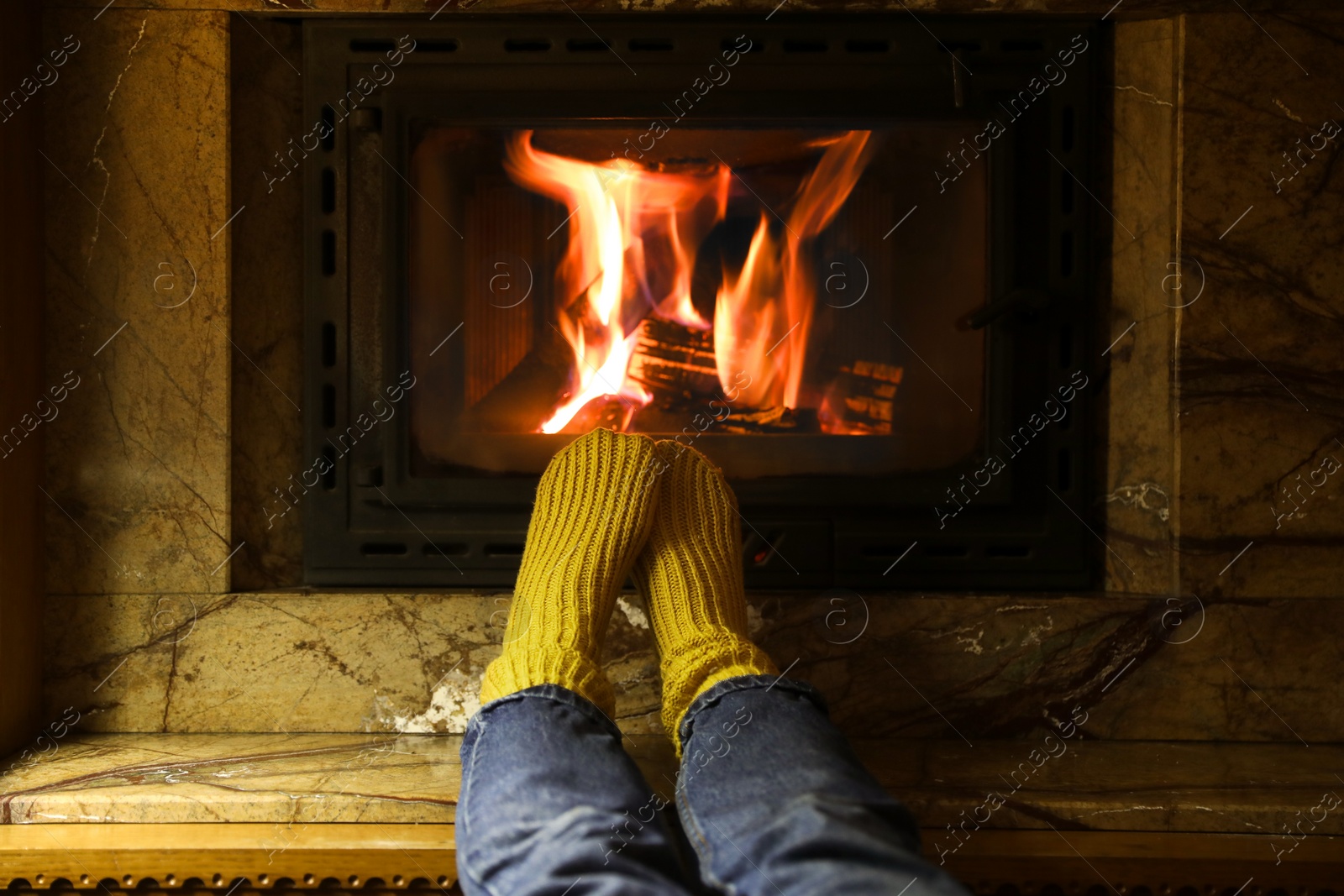 Photo of Woman in warm socks resting near fireplace indoors, closeup