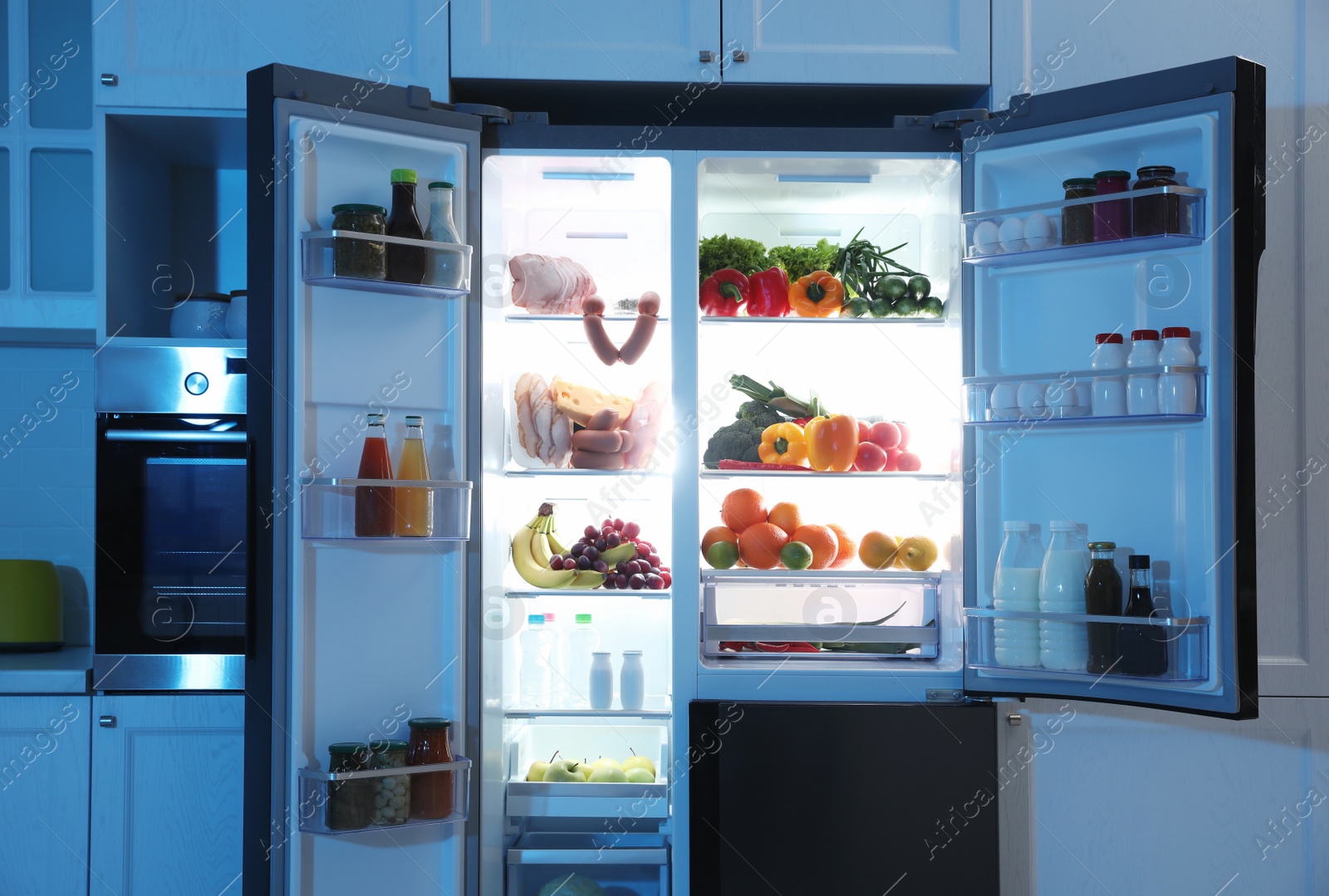 Photo of Open refrigerator filled with food in kitchen at night