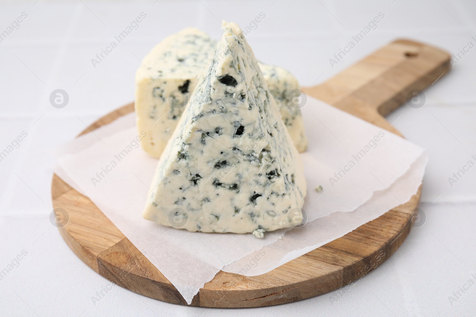 Photo of Wooden cutting board with blue cheese on white tiled table