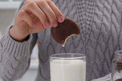 Photo of Woman dipping delicious choco pie into glass of milk, closeup