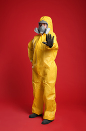 Photo of Woman in chemical protective suit making stop gesture on red background. Virus research