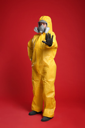 Woman in chemical protective suit making stop gesture on red background. Virus research