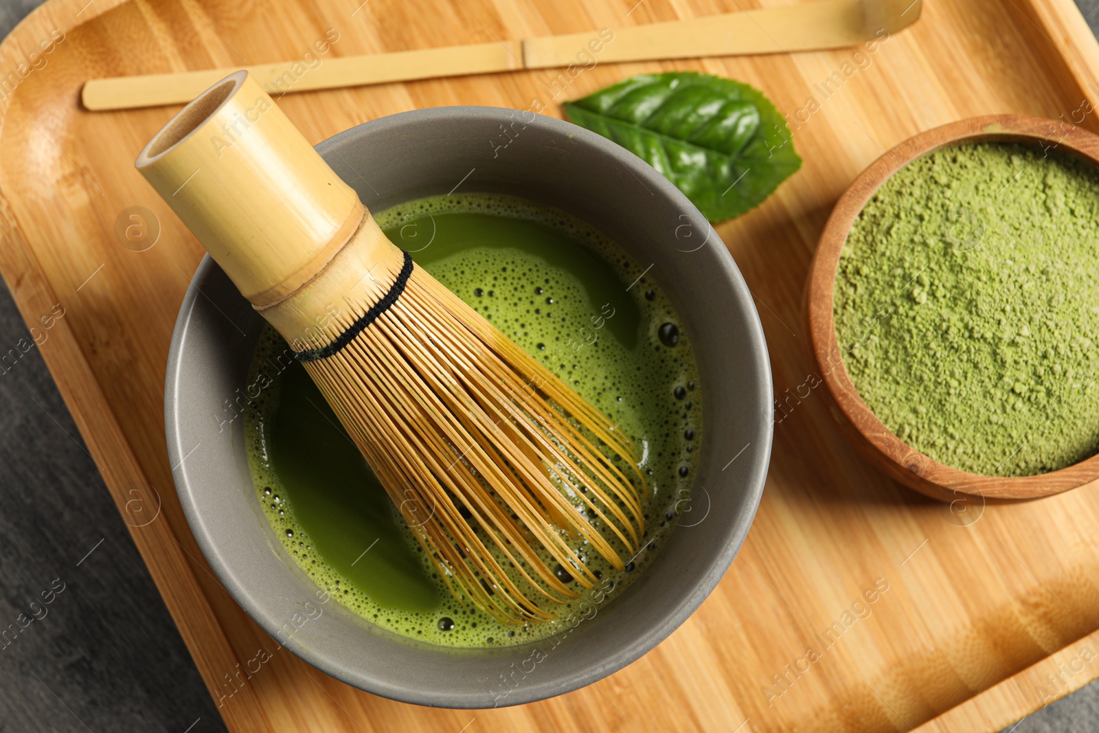 Photo of Cup of fresh matcha tea with bamboo whisk, green powder and spoon on table, top view