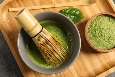 Photo of Cup of fresh matcha tea with bamboo whisk, green powder and spoon on table, top view