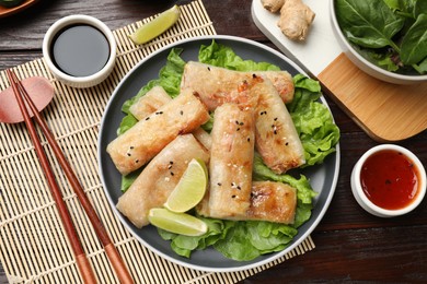 Photo of Tasty fried spring rolls, lettuce and sauce on wooden table, flat lay