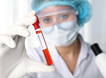 Photo of Scientist holding test tube with blood sample and label CORONA VIRUS in laboratory, focus on hand