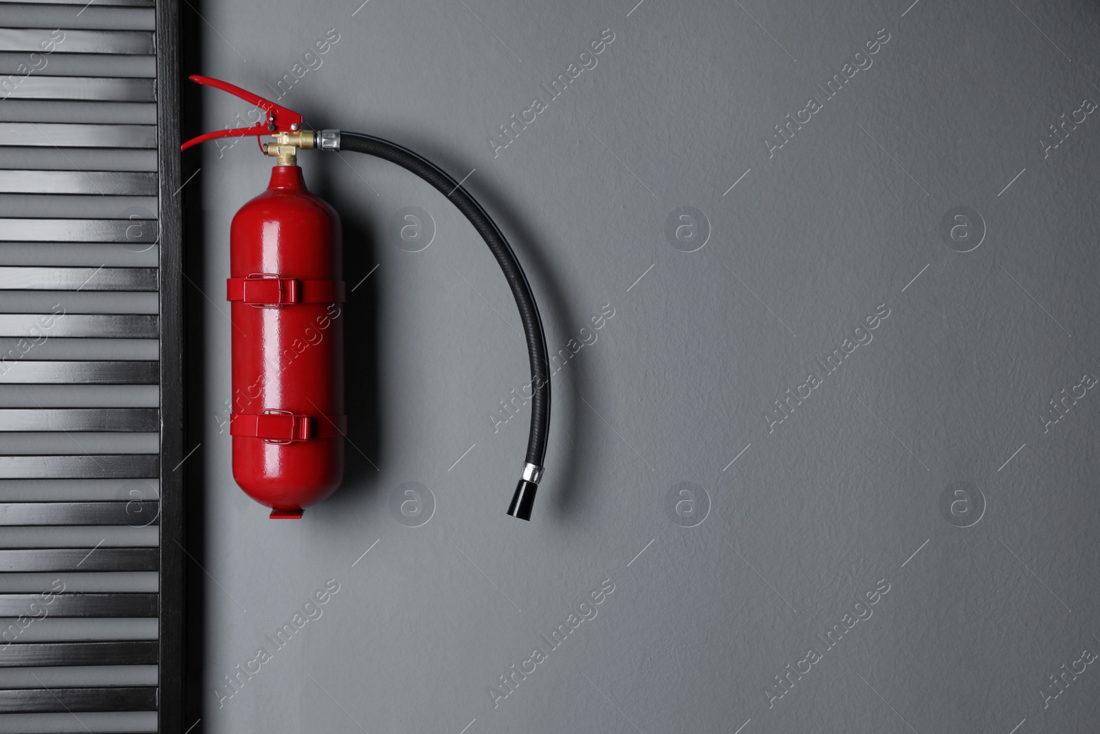 Photo of Fire extinguisher hanging on grey wall indoors. Space for text