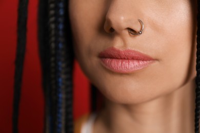 Photo of Young woman with nose piercing on red background, closeup