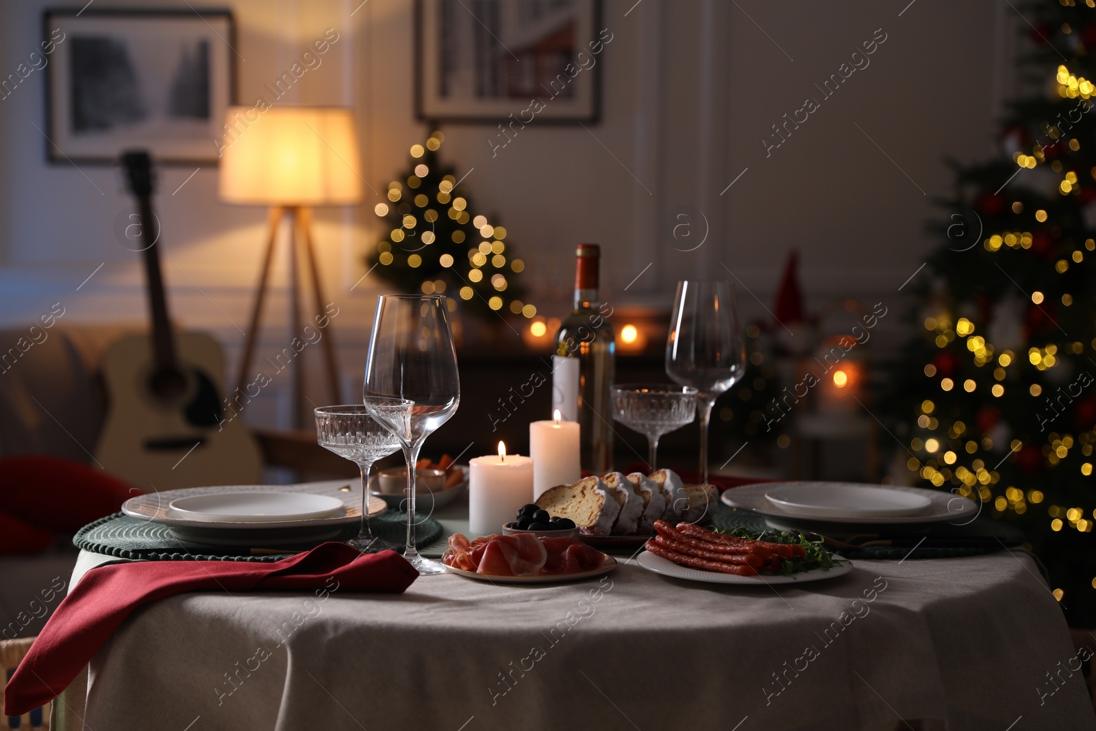 Photo of Christmas table setting with burning candles, appetizers and dishware in room