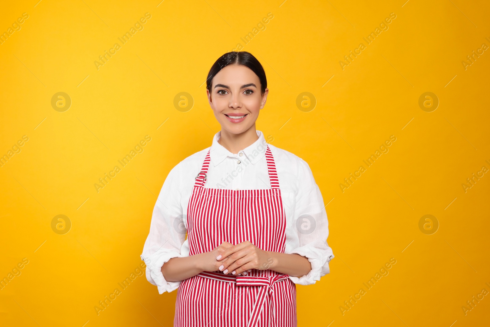 Photo of Young woman in red striped apron on yellow background