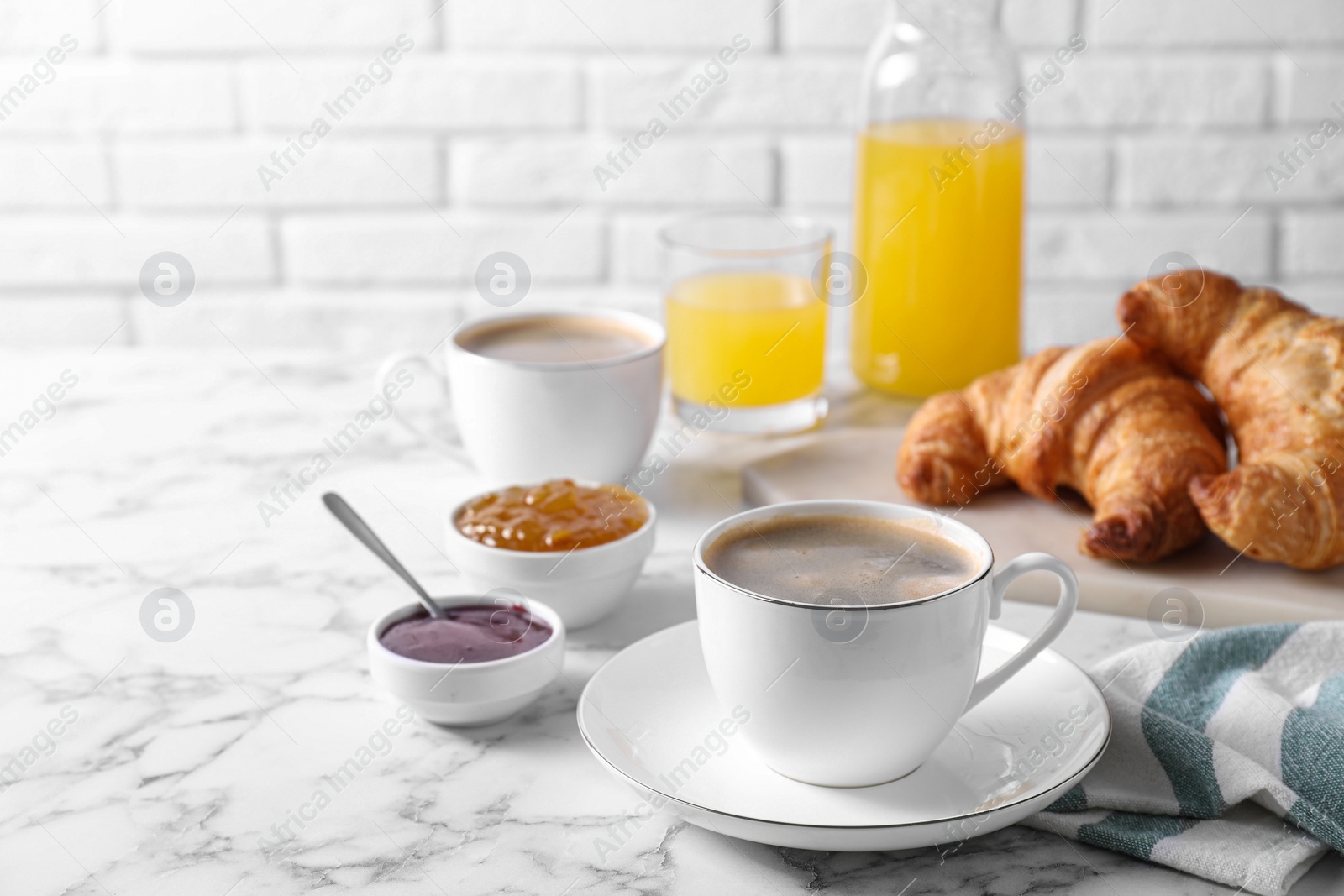 Photo of Tasty breakfast. Cups of coffee, fresh croissants and jam on white marble table, space for text