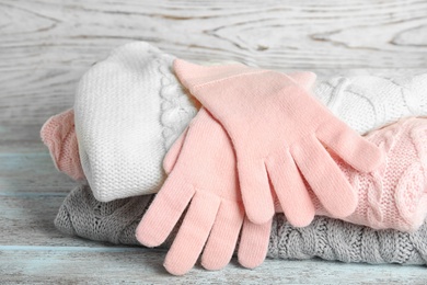 Photo of Stacked sweaters and gloves on wooden table, closeup. Autumn clothes