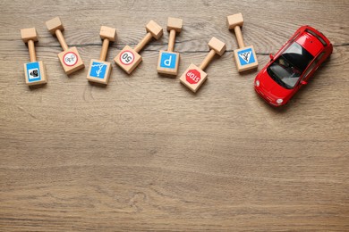 Photo of Many different miniature road signs and car on wooden background, flat lay with space for text. Driving school