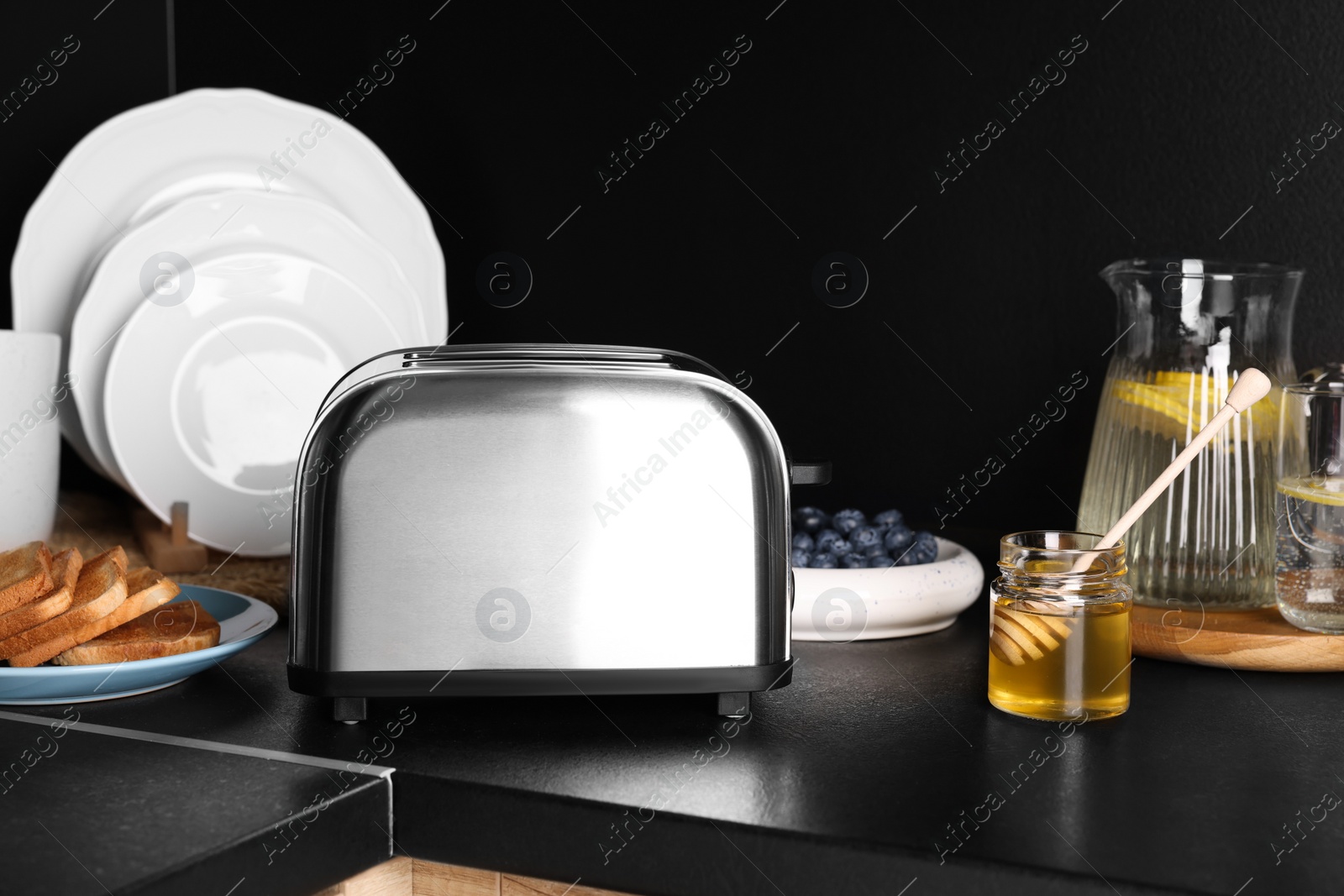 Photo of Toaster, roasted bread and honey on black countertop in kitchen
