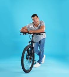 Photo of Handsome young man with modern bicycle on light blue background