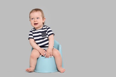 Photo of Little child sitting on baby potty against light grey background, space for text
