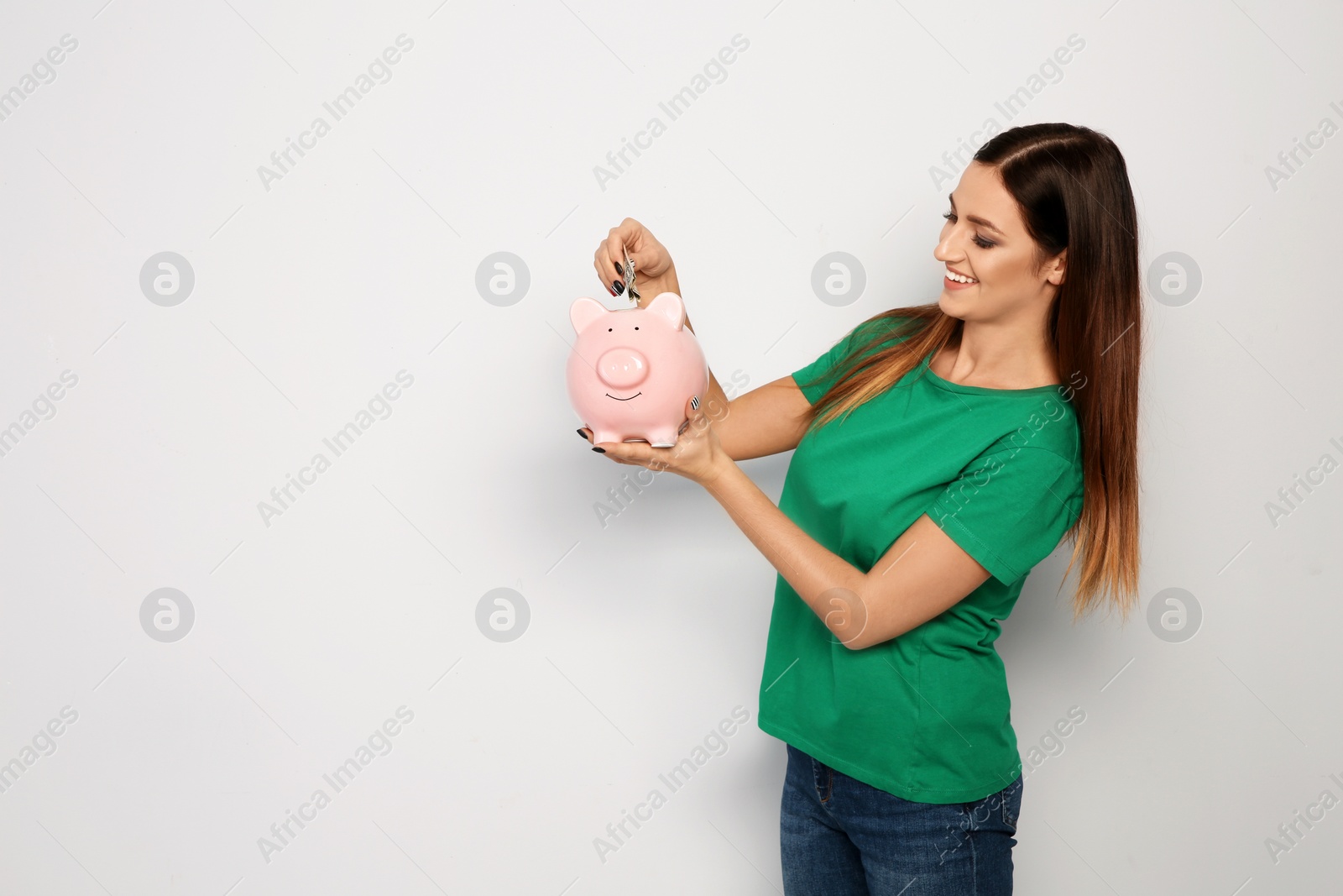 Photo of Young woman putting money into piggy bank on white background. Space for text