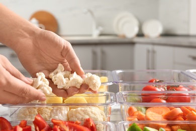 Photo of Woman putting cut cauliflower into box and containers with raw vegetables in kitchen, closeup