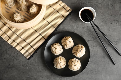 Photo of Flat lay composition with tasty baozi dumplings, bamboo steamer and soy sauce on grey table