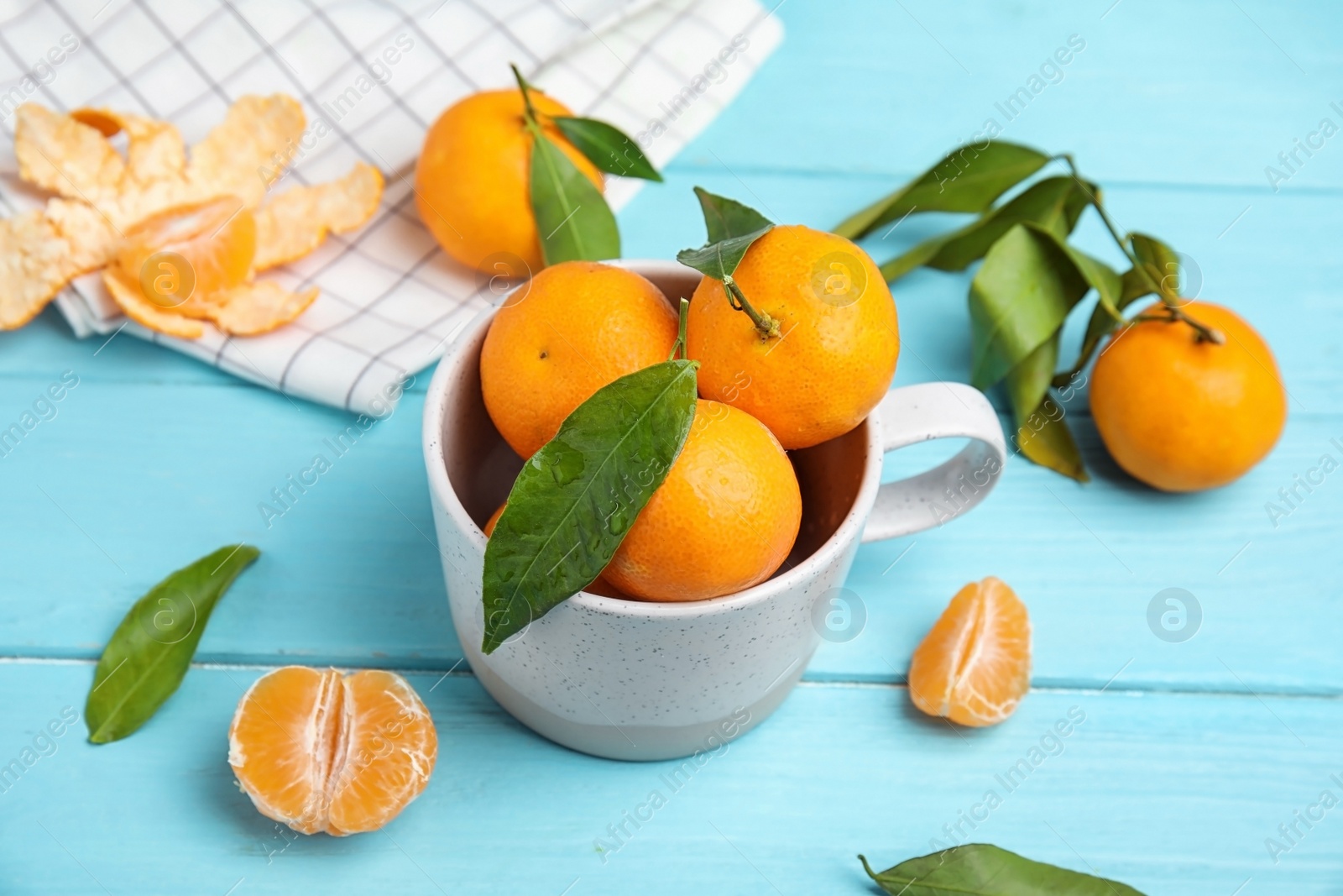 Photo of Fresh ripe tangerines with green leaves and mug on table