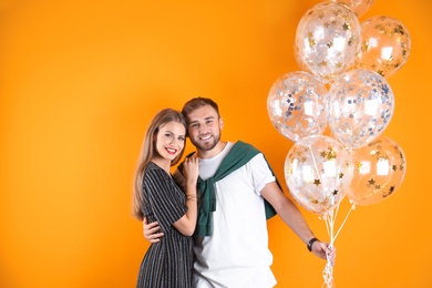 Young couple with air balloons on color background