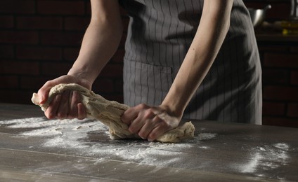 Making bread. Woman kneading dough at wooden table indoors, closeup