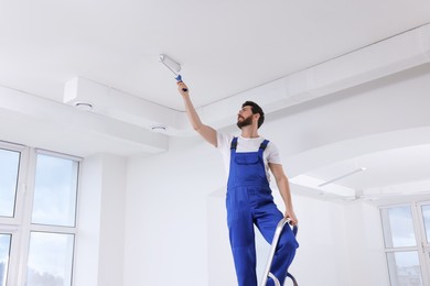 Photo of Handyman painting ceiling with roller on step ladder in room