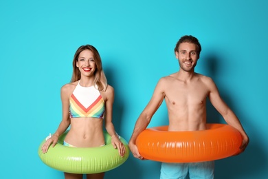 Photo of Happy young couple in beachwear with inflatable rings on color background
