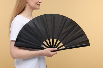 Woman with black hand fan on beige background, closeup