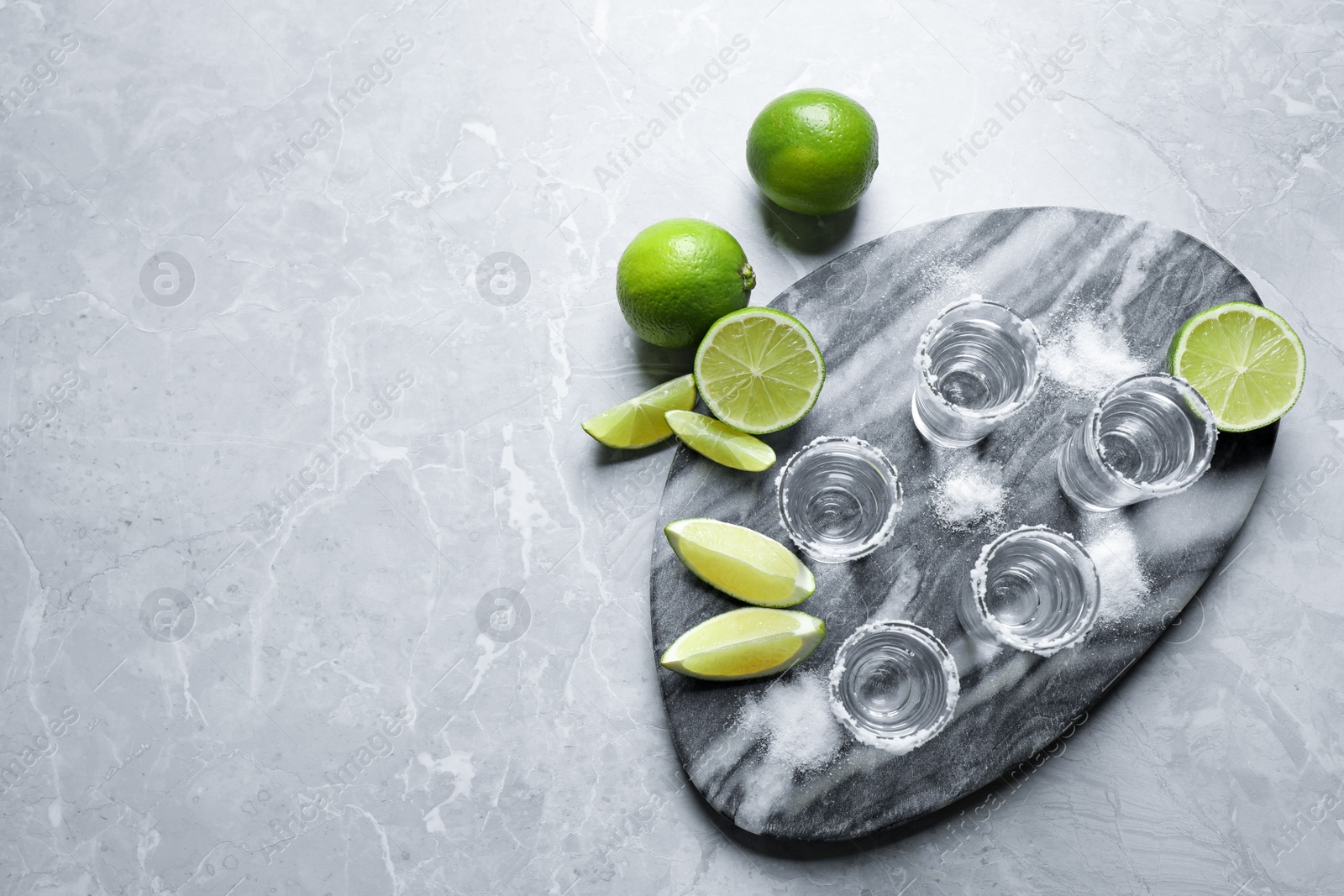 Photo of Mexican Tequila shots, lime slices and salt on grey marble table, flat lay. Space for text