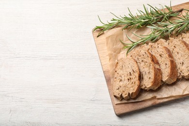 Photo of Cut buckwheat baguette with rosemary on white wooden table, top view. Space for text