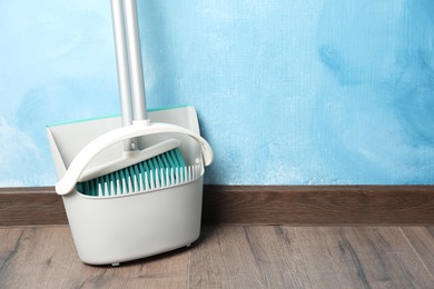 Photo of Plastic broom with dustpan near light blue wall indoors. Space for text