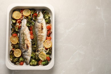 Photo of Delicious fish with vegetables and lemon in baking dish on light marble table, top view. Space for text