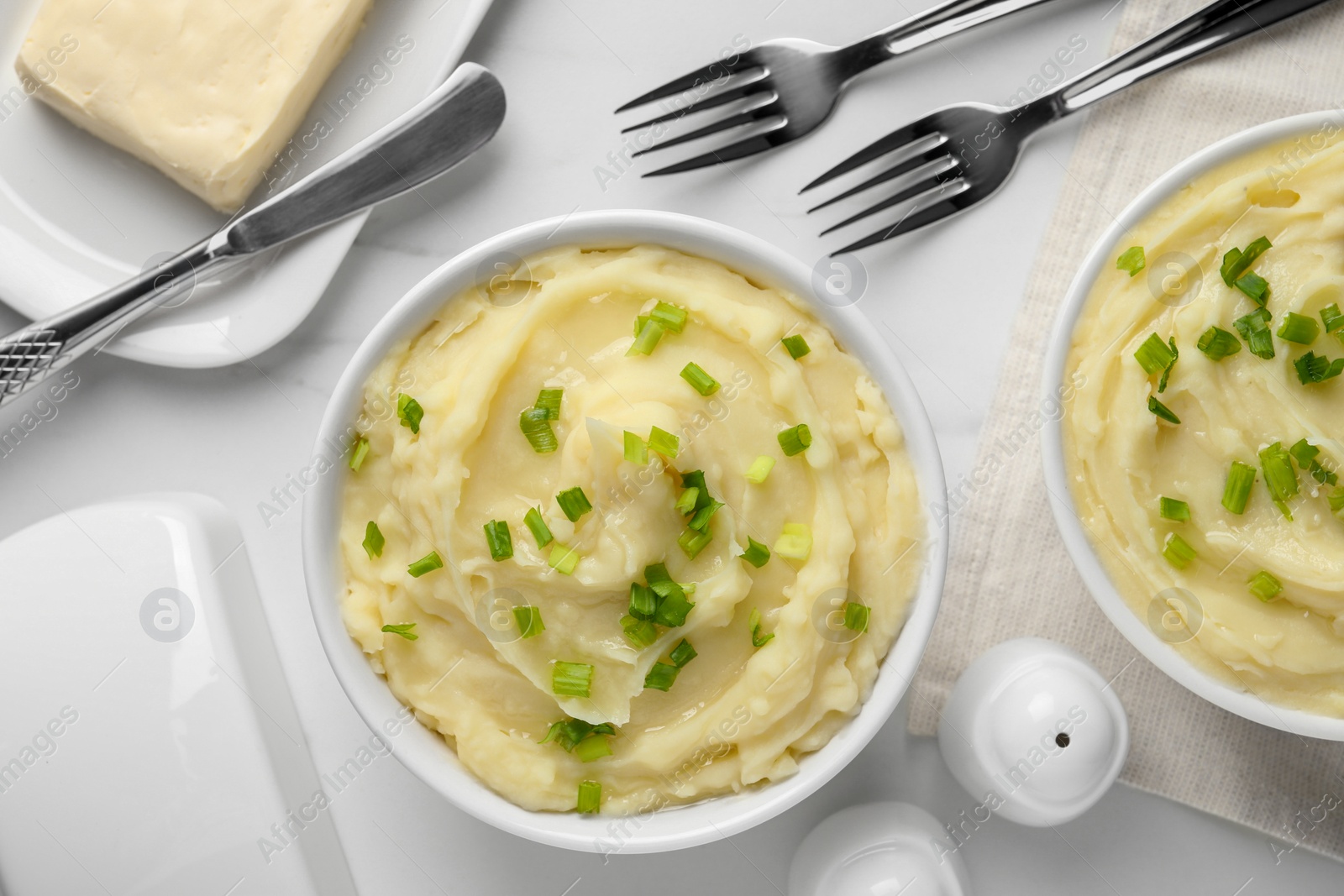 Photo of Bowls of delicious mashed potato with green onion on white table, flat lay